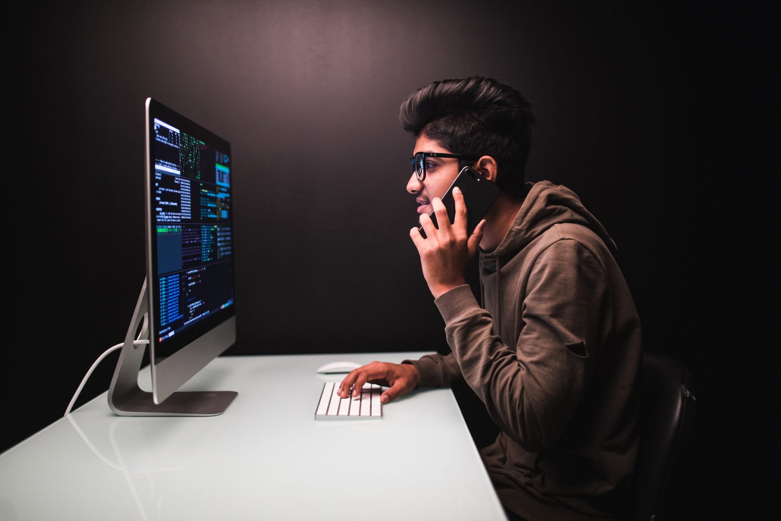 cybercrime, hacking and technology concept - male hacker with smartphone and coding on computers screen in dark room